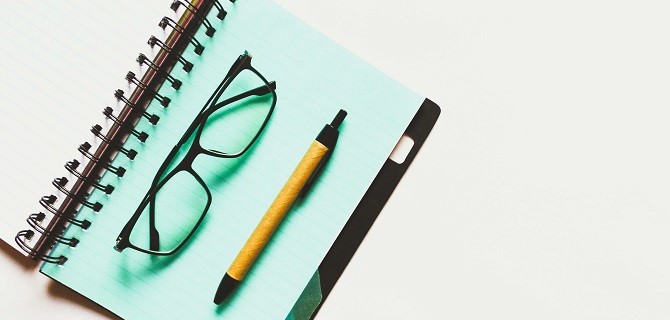 mintfarbenes Notizbuch mit schwarzer Brille und Kugelschreiber